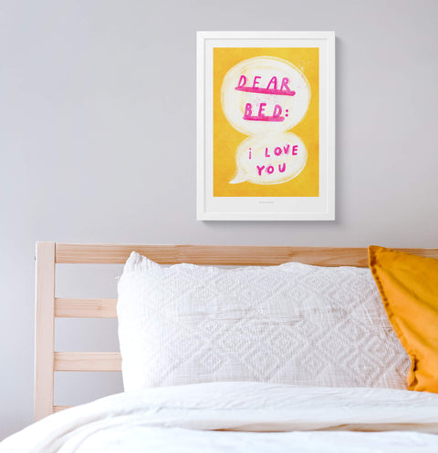 Fun bedroom print for above the bed featuring an illustrated speech bubble and hand painted typography quote saying "dear bed: I love you" with bright yellow and pink colors. The quote print is hanging above the bed.