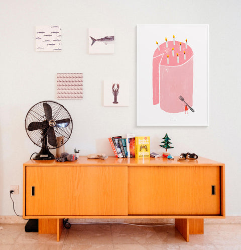 Pink birthday cake illustration poster featuring a big cake and a little woman wanting to eat the whole cake. This graphic art print is hanging in a fun and eclectic living room space.
