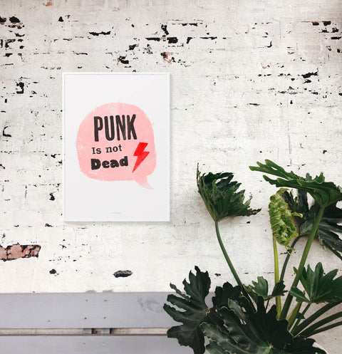 Retro music art print featuring the hand drawn phrase Punk is not dead in a pink illustrated speech bubble. This retro punk girl power print is hanging on a textured wall.