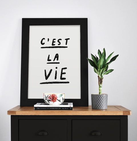 Cest la vie poster with black and white hand lettered typography in modern living room.