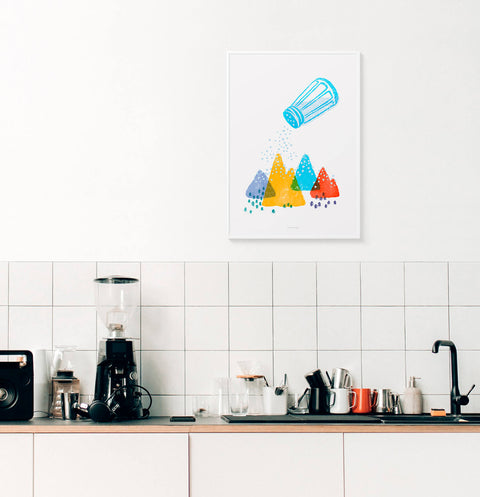 This funny kitchen wall art features a colorful illustration of mountains and a big salt shaker. Salt is falling like snow. This bright graphic art prints ins hanging in a white modern kitchen.