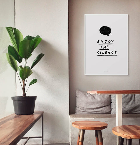 Black and white typography poster saying "enjoy the silence", inspired by the depeche mode song, hanging in neutral minimalist room decor.