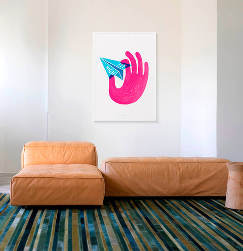 Motivational quote print hanging above sofa in modern minimalist living room. The quote wall art features an illustrated hand holding a paper plane with the inspirational words Fly high.