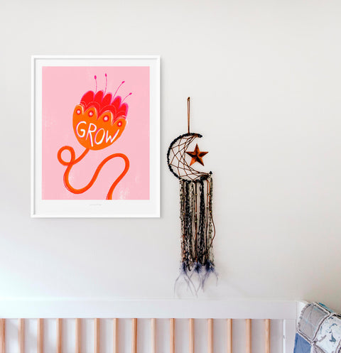 Inspirational wall art print hanging above crib in white baby nursery room featuring an illustration of an orange and pink flower with the hand lettered word Grow.