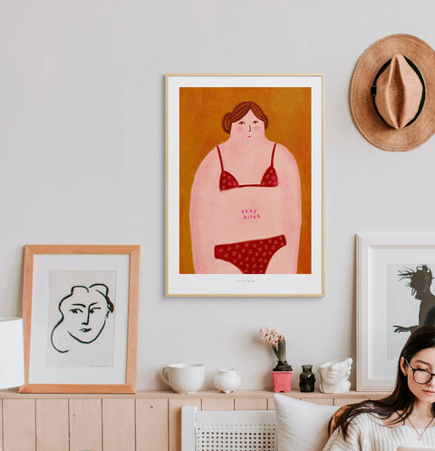 Body positive and feminist women wall art hanging in a bright and contemporary interior and featuring an illustration of a curvy woman in bikini and the phrase sexy bitch.