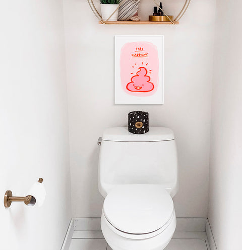 Shit happens is a funny toilet art featuring an illustration of a pink poo and a hand drawn quote saying shit happens. This funny bathroom print is hanging above a toilet.