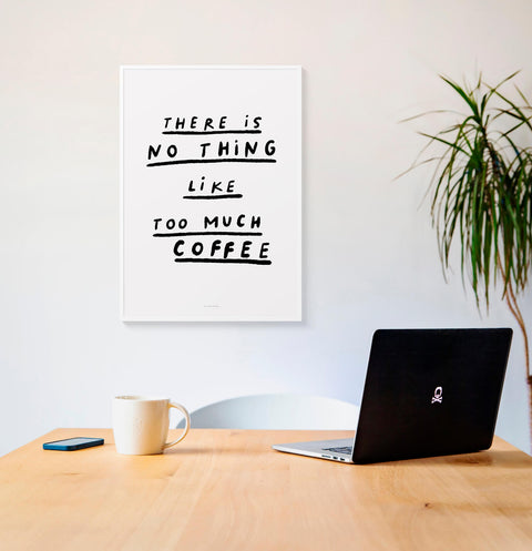 Modern coffee wall art for caffeine lover. Quote print with black and white hand lettered typography saying "There is no such thing like too much coffee" hanging above a desk in a minimalist office space.